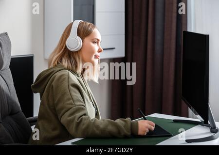 Giovane donna graphic designer freelance impegnato a lavorare da casa utilizzando un pc e un tablet grafico nell'interno del salotto. Adolescente casual g Foto Stock