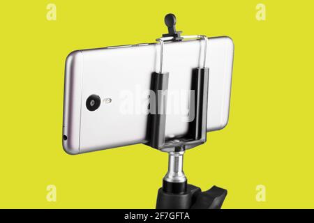 Smartphone collegato a un treppiede su sfondo giallo. Concetto di selfie e blogging Foto Stock