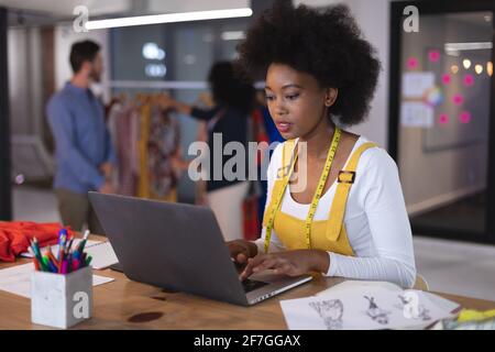 Donna americana stilista di moda che indossa una metro a nastro su misura utilizzando un computer portatile pensare Foto Stock