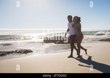 Felice coppia afroamericana che cammina sulla spiaggia abbracciando Foto Stock