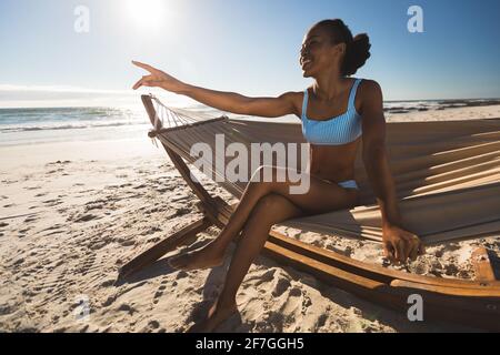 Donna afro-americana felice seduta in amaca sulla spiaggia puntando Foto Stock