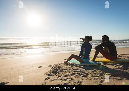 Felice coppia afroamericana sulla spiaggia seduta sulle tavole da surf guardando verso il mare Foto Stock