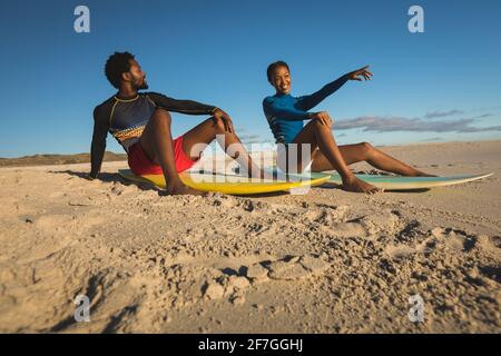 Felice coppia afroamericana sulla spiaggia seduta sulle tavole da surf puntamento Foto Stock