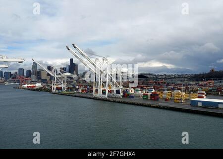 Terminal per container con gru a portale situato a Seattle, Washington, USA con profilo di grattacieli sullo sfondo sotto il suggestivo cielo coperto. Foto Stock
