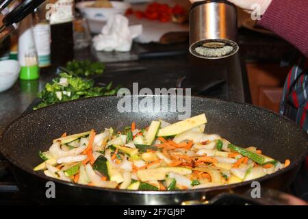 Un primo piano di qualcuno che aggiunge pepe alle verdure in una padella. Fondo del mulino del pepe e piccola parte della persona che lo usa in cornice. Foto Stock