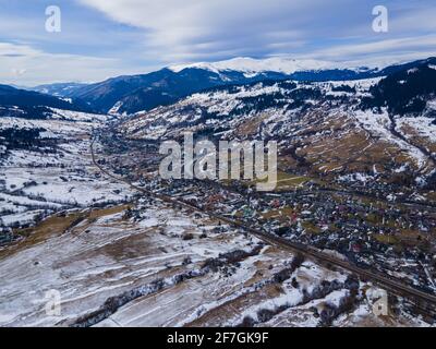 Splendida vista dal drone al paesaggio in montagne Carpazi innevate con villaggio, strada, fiume, foresta e cielo. Foto Stock