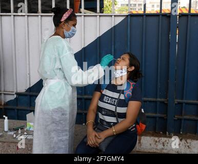 Mumbai, India. 07 aprile 2021. Un operatore sanitario che indossa una tuta per dispositivi di protezione individuale (DPI) raccoglie un campione di tampone nasale da una donna all'arrivo in treno a Dadar Terminus. I passeggeri che arrivano in treno a Mumbai dallo stato del Gujarat sono sottoposti a screening per il livello di ossigeno, la temperatura e, se si riscontra essere affetti da febbre, devono essere sottoposti a test con tampone presso la stazione ferroviaria prima di essere autorizzati a procedere alla loro rispettiva destinazione. (Foto di Ashish Vaishnav/SOPA Images/Sipa USA) Credit: Sipa USA/Alamy Live News Foto Stock
