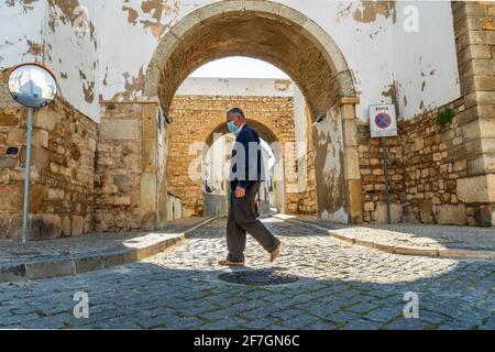 Faro, Portogallo - 24 marzo 2021: Uomo con maschera a piedi lungo le mura medievali di Faro, Algarve, Portogallo meridionale Foto Stock