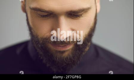 Studio primo piano ritratto di bell'uomo bearded guardando verso il basso con gli occhi a metà chiusi Foto Stock