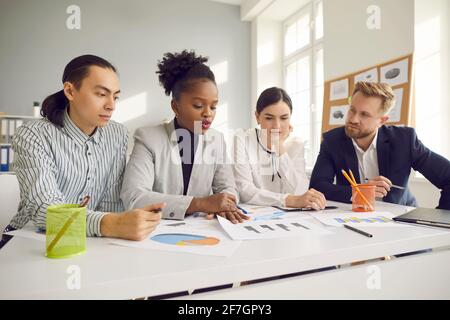 Team di giovani imprenditori che lavorano con documenti e discutono ulteriormente strategia aziendale Foto Stock