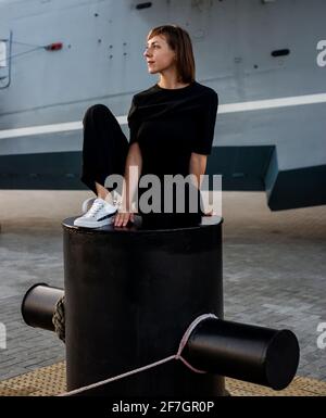 Donna è seduta sul molo nel porto in sneakers Foto Stock
