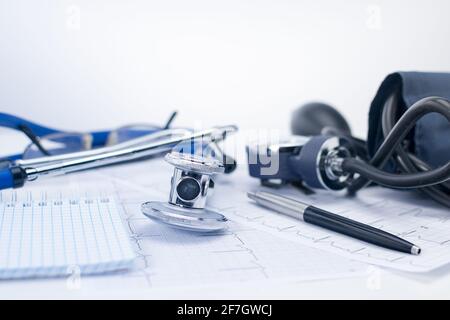Stetoscopio sul tavolo di lavoro di un cardiologo. Tonometro, elettrocardiogramma e blocco note con occhiali, concetto medico Foto Stock
