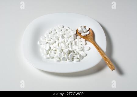 Molte pillole bianche in piatto bianco con cucchiaio di legno per la cena. Concetto medico. Foto Stock