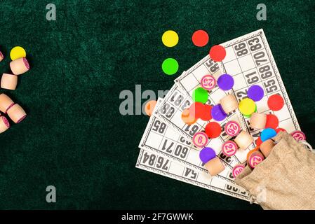 Lotto, classico gioco da tavolo per famiglie. Botti di legno in juta, tessere e patatine colorate su una superficie di velluto verde. Vintage game, bingo. Foto Stock