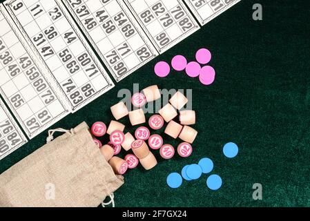 Lotto, classico gioco da tavolo per famiglie. Alcune botti di legno, scaglie blu e carte sulla superficie verde di velluto. Vintage game, bingo. Foto Stock