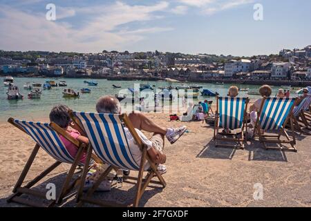 I vacanzieri seduti in sedie a sdraio intorno al porto di St. Ives, Cornovaglia, Regno Unito Foto Stock