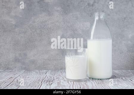 Bicchiere in vetro con latte e bottiglia di latte su una tavolo in legno su sfondo grigio con spazio per la copia Foto Stock