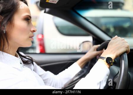 La giovane donna in una camicia si siede al volante di una macchina Foto Stock