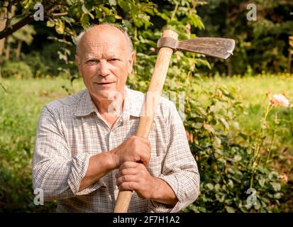 Ritratto dell'uomo anziano con l'ascia sulla spalla in giardino. Foto Stock