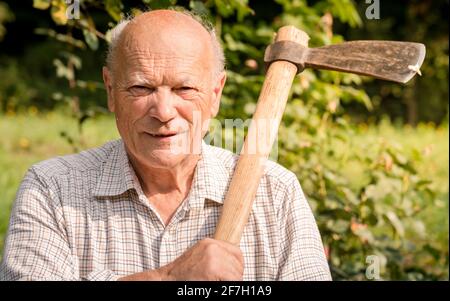 Ritratto dell'uomo anziano con l'ascia sulla spalla in giardino. Foto Stock