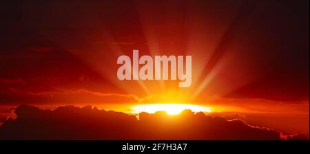 Maestoso tramonto con luminosi raggi solari sul cielo rosso. Foto Stock