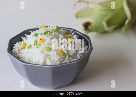 Riso bianco al vapore cosparso di cipolle primaverili e mais dolce. Un pranzo sano e veloce. Scatto su sfondo bianco Foto Stock