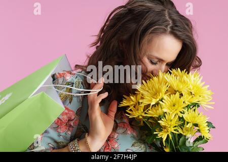 donna felice di 40 anni con lunghi capelli di brunetta ondulati con fiori di crisantemi gialli e borsa verde su sfondo rosa. Foto Stock