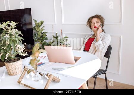 Una donna freelance affaccendata ed elegante sta usando lo smartphone, avendo una conversazione seria. Attraente giovane donna d'affari che discute con i colleghi un progetto Foto Stock
