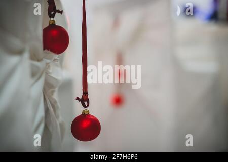 Palla rossa di natale appesa alla schiena di una sedia bianca su una cena di gala di natale o di Capodanno. Particolare di ornamenti in christampa rossa su un sedile. Foto Stock