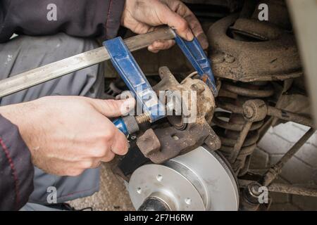 Comprimere una pinza del freno di una vettura, spingendo il pistone con una morsa a carpentiere che funge da asta di spinta. Riparazione del vecchio freno dell'automobile usando gli attrezzi dilettanti. Foto Stock