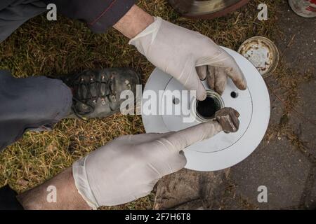 Martellare la nuova bronzina o la nuova pista nel mozzo dell'auto e nel disco del freno con un martello o un mazzuolo. Meccanico domestico che fissa i cuscinetti della ruota su un'automobile. Vista dall'alto Foto Stock