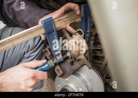 Comprimere una pinza del freno di una vettura, spingendo il pistone con una morsa a carpentiere che funge da asta di spinta. Riparazione del vecchio freno dell'automobile usando gli attrezzi dilettanti. Foto Stock