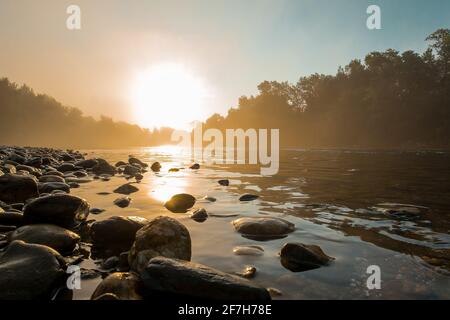 Misty panorama frizzante di un fiume e riva del fiume con ciottoli nelle prime ore del mattino. Ambiente mistico durante un'ora del mattino presto. Foto Stock