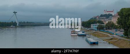 Moody panorama della città di Bratislava vista dal ponte verso il castello e Novy ponte sul fiume in una giornata di grigio opaco. Foto Stock