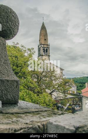 Vista verso il vecchio campanile nel villaggio di Stanjel, Slovenia in una romantica giornata di pioggia con fitte nuvole che si innalzano sopra il cielo Foto Stock