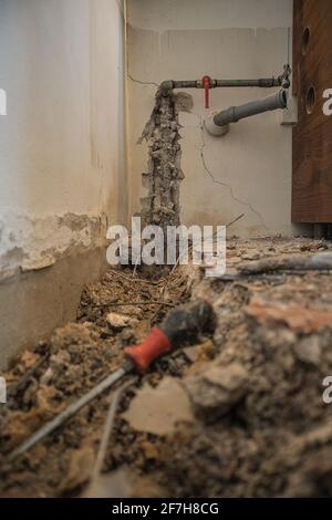 Rottura del tubo dell'acqua in un appartamento. Foro visibile nel terreno con piastrelle, calcestruzzo vecchio e detriti. Cantiere mentre provando a rimediare una lla di acqua Foto Stock