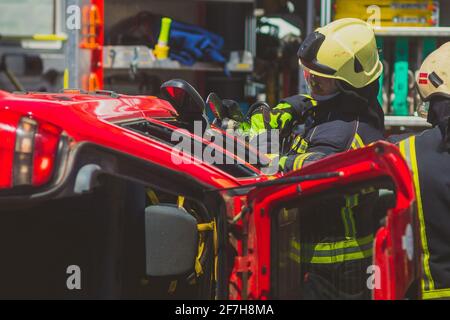 Vigili del fuoco che usano una mascella idraulica o forbici per tagliare la macchina schiantata aperta per salvare il conducente intrappolato dentro. Situazione di emergenza in una strada cr Foto Stock