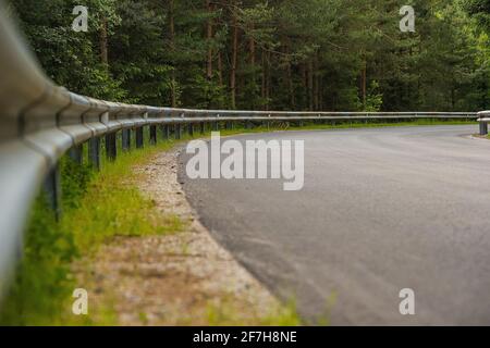 Strada asfaltata in campagna con ringhiera o recinzione in metallo su una curva. Strada aperta con alberi intorno e concentrarsi sulla barriera di sicurezza sul lato. Foto Stock