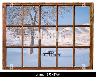 Tavolo da picnic coperto da neve fresca ai piedi delle Montagne Rocciose Mattina come visto da una finestra d'epoca Foto Stock