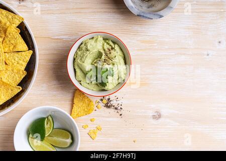 Hummus dip avocado e patatine di mais su tavolo di legno bianco, vista dall'alto, antipasto messicano tradizionale in ciotola di ceramica Foto Stock