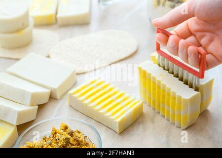 Processo di taglio con sapone fai da te. Saponetta artigianale con erbe e fiori. Sapone artigianale eco hobby fatto a mano su tavola bianca. Molti giallo bianco vari Foto Stock