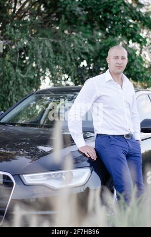 bell'uomo calvo in un vestito vicino auto di lusso. uomo d'affari in automobile Foto Stock