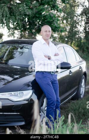 bell'uomo calvo in un vestito vicino auto di lusso. uomo d'affari in automobile Foto Stock