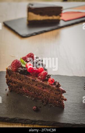 Un bel lampone al cioccolato e una torta al mirtillo serviti su un piatto di pietra. Un'altra torta sullo sfondo. Foto Stock