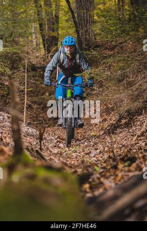 Pedalando in discesa con una moderna bicicletta elettrica o mountain bike in autunno o in inverno in un bosco. E-ciclista moderna in legno. Foto Stock