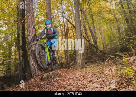 Pedalando in discesa con una moderna bicicletta elettrica o mountain bike in autunno o in inverno in un bosco. E-ciclista moderna in legno. Foto Stock