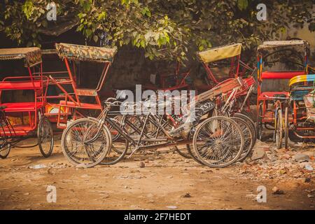 Biciclette parcheggiate risciò in india, moltitudine di risciò di colore rosso e biciclette in attesa di essere utilizzato su un parcheggio di ghiaia. Foto Stock