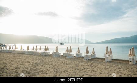 Spiaggia con edifici per gli hotel vicino alla baia con bianco barche e barche con palme verdi sullo sfondo di un cielo nuvoloso Foto Stock