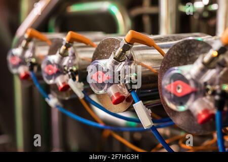 Elementi per la preparazione e il filtraggio della birra. Valvole con fili e tubi flessibili collegati. Una fila di valvole, una affilata l'altra in messa a fuoco morbida. Foto Stock