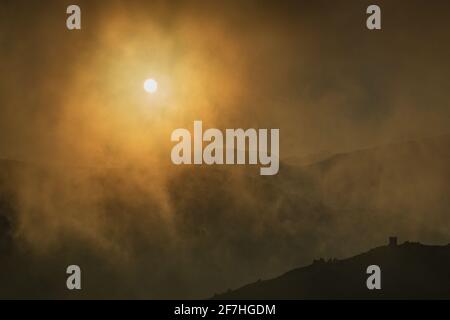 Sole nascosto dietro nubi nebbie sulla cima della montagna. Sole dorato che splende attraverso le montagne coperte di nebbia, nuvole o nebbia nelle ore serali. SIL Foto Stock